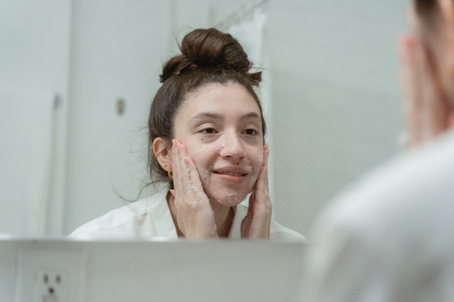 Close-up of a woman applying a facial cleanser to her combination skin, showing both oily and dry areas.