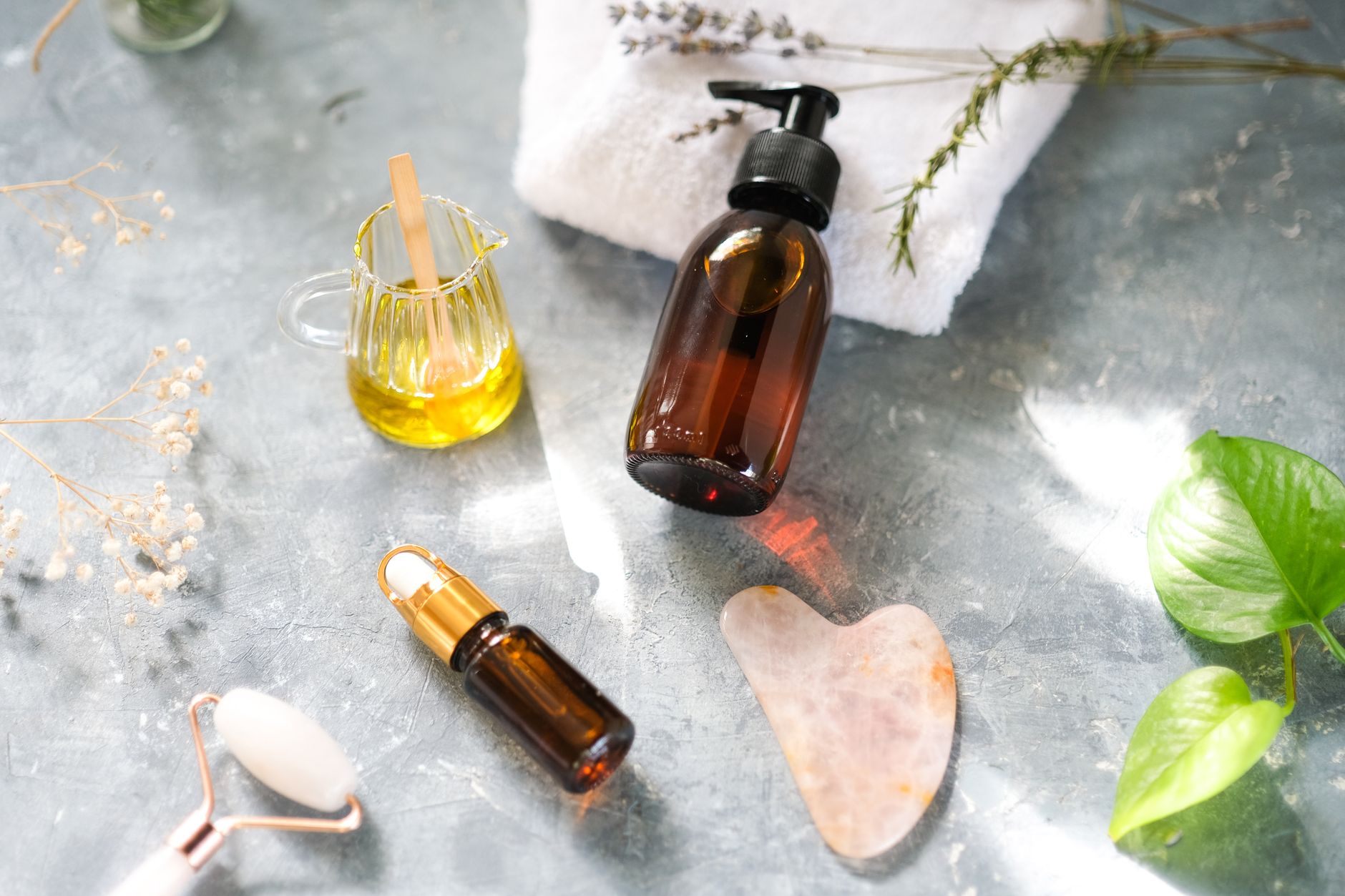 A close-up of various facial oils in dropper bottles with natural elements like leaves and petals.