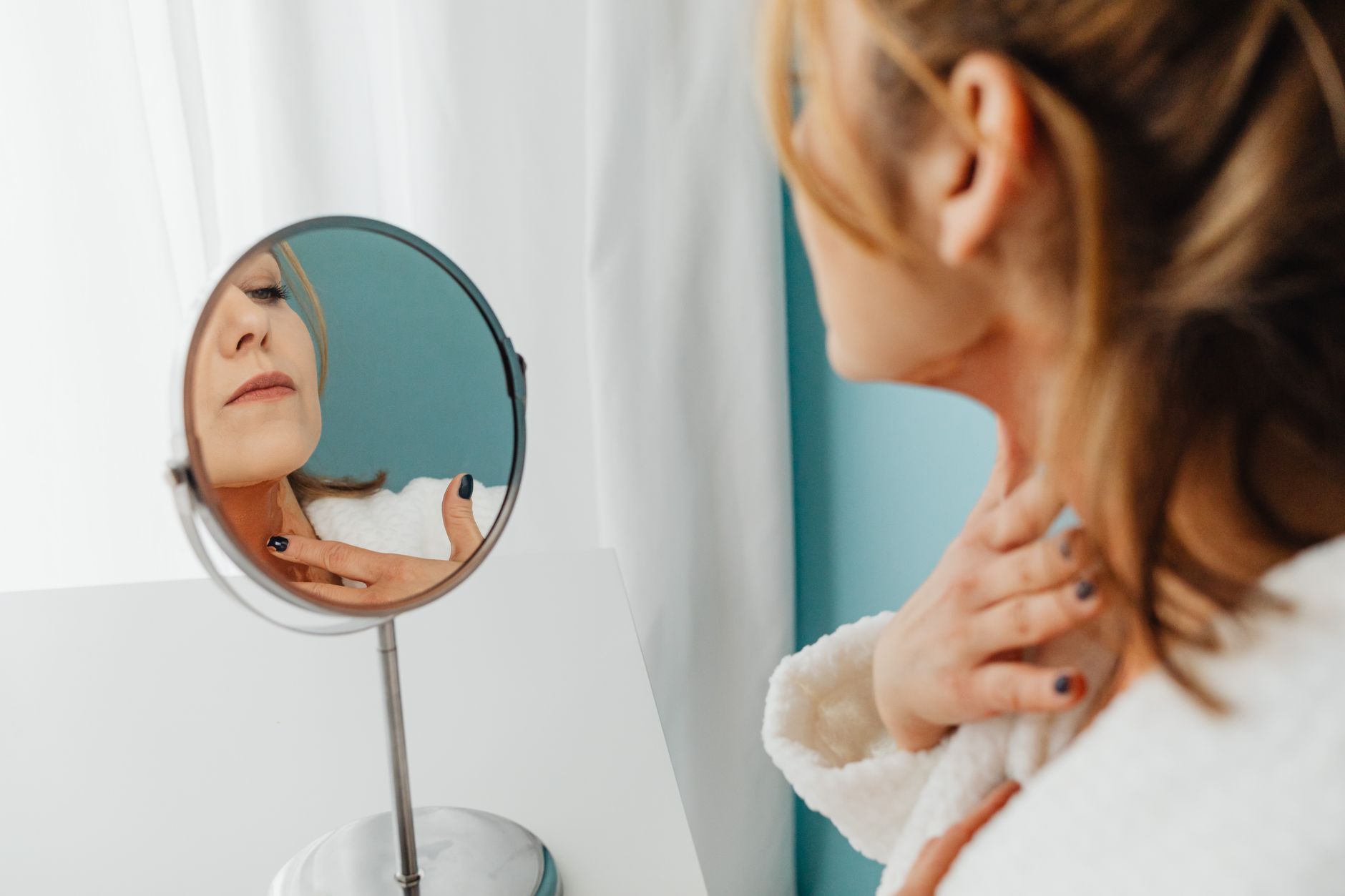 A woman gently applying cream to her neck, showcasing the importance of neck care.