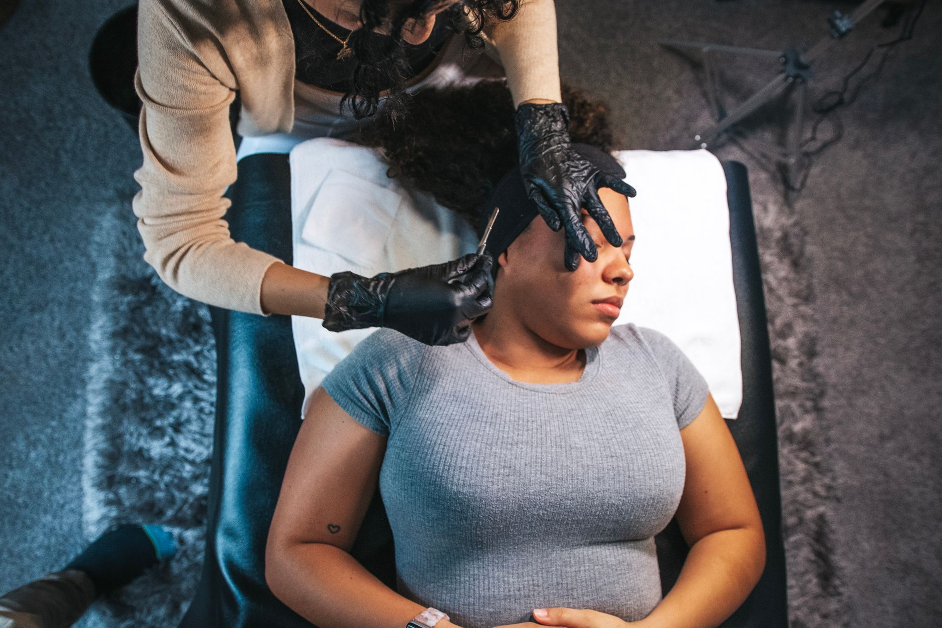 A woman gently holding a dermaplaning tool to her cheek, with a soft focus background of skincare products.
