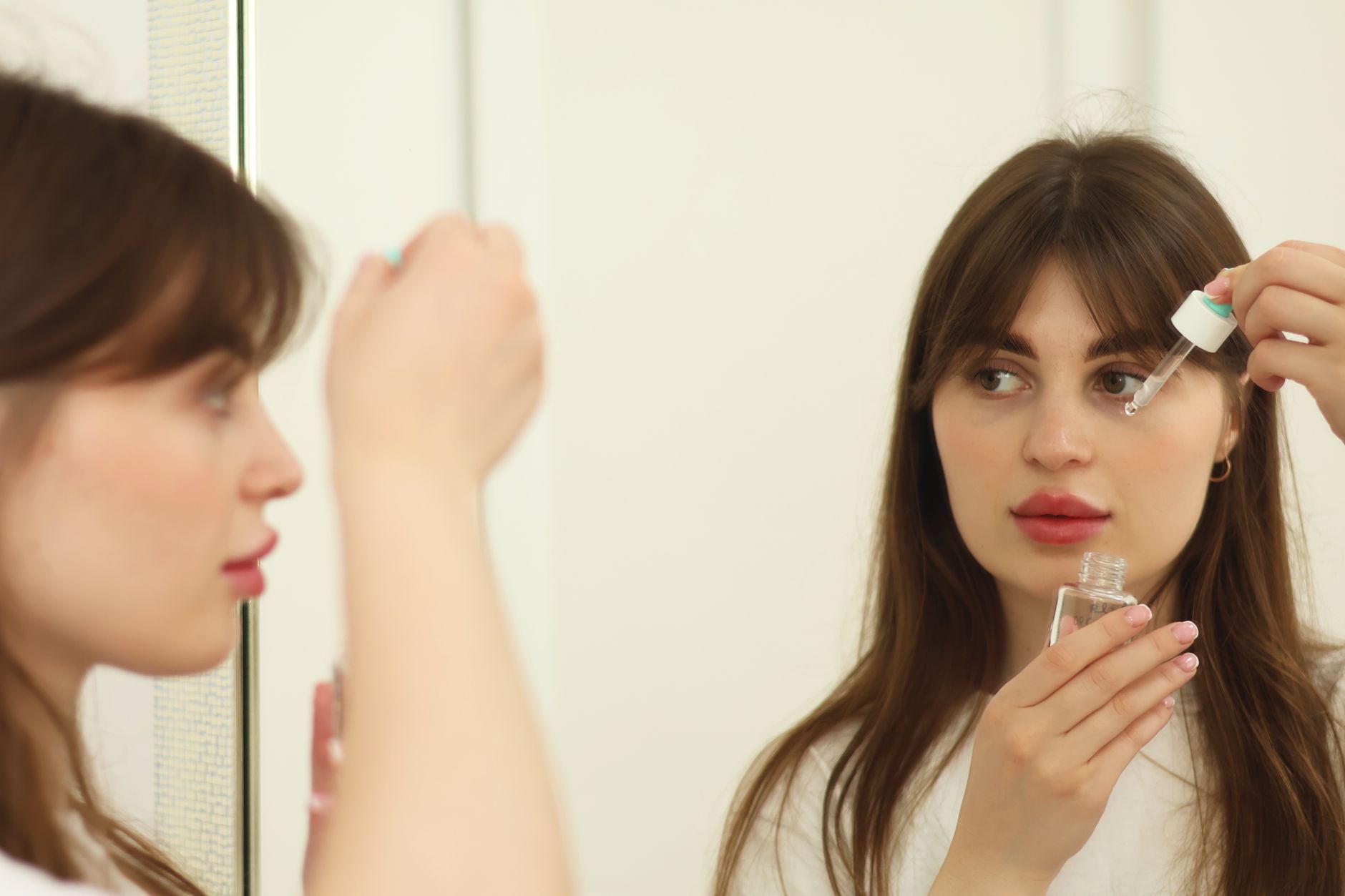 A woman with clear, glowing skin looking thoughtfully at a skincare product.