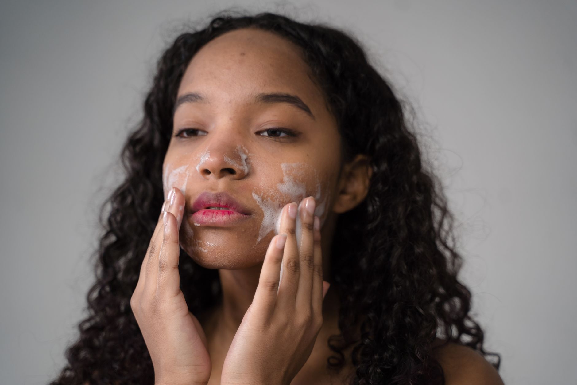 A person performing the double cleansing skincare routine with oil and foam cleansers.